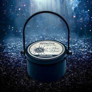 May include: A black metal container with a handle, labeled "Salem's Best Apothecary by J&M Soy Candles" and "Pixie Dust 100% Pure Superior Quality". The container is sitting on a blue and black sparkly surface.