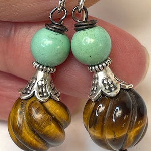May include: A pair of dangle earrings featuring round, light green beads topped with silver-toned metal bead caps and ribbed, spherical tiger's eye gemstones. The components are connected by dark wire wraps and silver-toned earring hooks.
