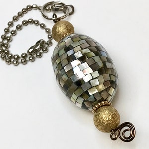 Könnte beinhalten: Eine silberne Kette mit einer goldenen und schillernden Mosaikperle und einer goldenen Perle mit strukturierter Oberfläche. Die Kette hat oben einen Ring zum Aufhängen.