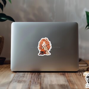 Puede incluir: Una pegatina con una ilustraci&oacute;n de dibujos animados de una joven con el pelo largo y rizado de color naranja que lleva un abrigo marr&oacute;n y botas. Est&aacute; sonriendo y se lleva la mano a la mejilla. La pegatina est&aacute; en un port&aacute;til plateado.