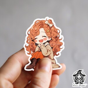 Puede incluir: Una pegatina con una ilustraci&oacute;n de dibujos animados de una ni&ntilde;a joven con el pelo largo y rizado de color naranja que lleva un jersey marr&oacute;n y pantalones naranjas. Est&aacute; sonriendo y tiene las manos juntas delante de ella. La pegatina est&aacute; sobre un fondo blanco.