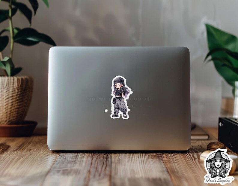 Puede incluir: Una pegatina con una ilustraci&oacute;n de dibujos animados de una persona joven que lleva un atuendo blanco y negro y un sombrero negro. La pegatina est&aacute; en un ordenador port&aacute;til.