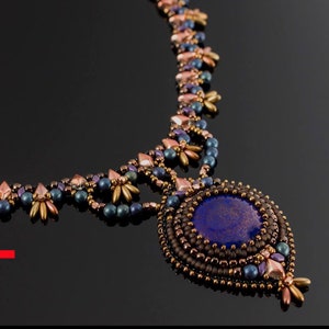 May include: A beaded necklace kit featuring a large, round, blue gemstone pendant. The necklace is crafted with brown, gold, and purple beads. The kit contains all the beads and instructions required to make the necklace. The text "KIT" is in large red letters at the bottom of the image.