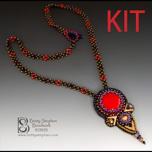 Puede incluir: Un collar de cuentas hecho a mano con un llamativo colgante rojo. El collar presenta cuentas rojas, moradas y doradas. La palabra "KIT" se muestra en rojo. Diseñado por Betty Stephan Beadwork.