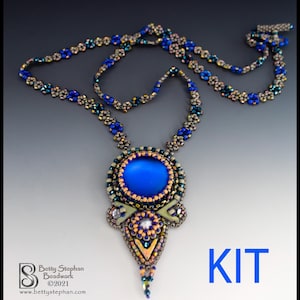 Puede incluir: Un collar de cuentas hecho a mano con una piedra central azul grande y redonda. El collar presenta un intrincado trabajo de cuentas en tonos de azul, dorado y colores iridiscentes. La palabra "KIT" se muestra en texto azul.