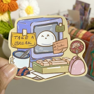 May include: A sticker featuring a cartoon illustration of a computer with a white face and the text "Take a Break" on a yellow note. The computer has a keyboard, a pink phone, and a cup of coffee.