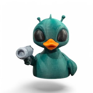 May include: A teal blue duck with large black eyes and an orange beak holding a gray toy gun. The duck has two antennas on its head.