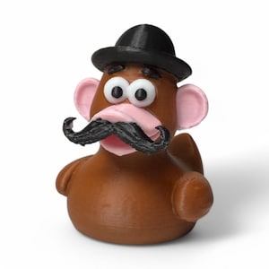 May include: A brown rubber duck with a black bowler hat, a black mustache, and pink ears. The duck has large, white eyes with black pupils.