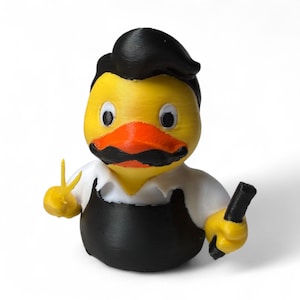 May include: A 3D-printed novelty duck figurine with a yellow body, orange beak, and black mustache. The duck wears a black apron and white shirt, holding a black object in one hand and a peace sign with the other.