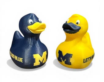May include: Two rubber duck toys, one navy blue and one yellow. Each duck has a large letter "M" and text that reads "GO BLUE" and "LET'S GO". The ducks have yellow and black beaks.
