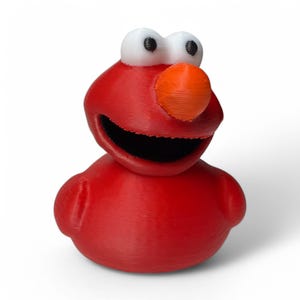 May include: A 3D-printed red character with white eyes, a black mouth, and an orange nose. The character has a round body and a smiling expression. The toy is a recognizable character from a children's television show.