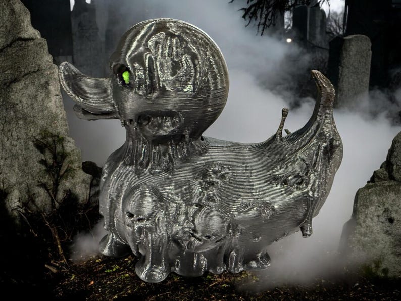 May include: A black rubber duck with a dripping, melted appearance. The duck has a green eye and is set against a dark, foggy background.
