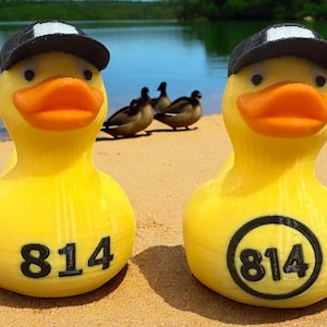 May include: Two yellow rubber duckies with black baseball caps and the number 814 printed on them. One duckie has the number printed in a circle.
