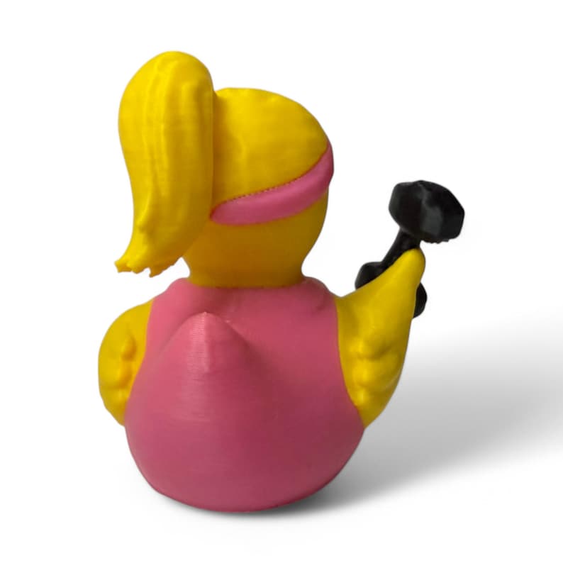 K&ouml;nnte beinhalten: Eine gelbe Gummiente mit einem rosafarbenen Stirnband und einer schwarzen Hantel in der Hand. Die Ente tr&auml;gt ein rosa Shirt.