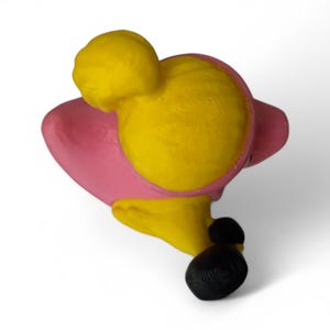 K&ouml;nnte beinhalten: Eine rosa und gelbe 3D-gedruckte Figur eines Menschen mit einem Dutt. Die Figur tr&auml;gt ein rosa Kleid und schwarze Schuhe.