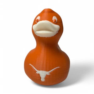 May include: Orange duck figurine with white accents on the beak, eyes, and a Longhorn logo on the body. The duck is a novelty item, likely a decorative piece or a collectible. The figurine is made of a solid material.
