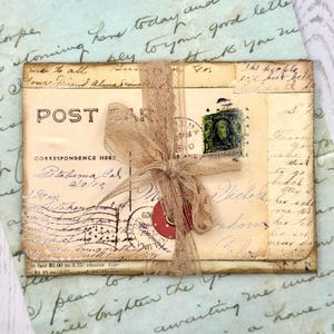 May include: A vintage postcard with the word "POST" printed on the front, tied with a beige ribbon. The postcard has handwritten text, a postage stamp, and a red circular tag. The background is a light blue paper with handwritten script.
