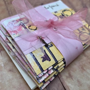 May include: A stack of blank note cards tied with a pink ribbon and a key charm. The cards feature a vintage-inspired design with keys and other decorative elements.
