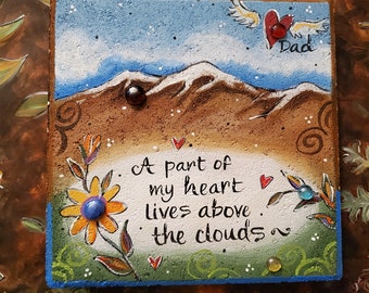 May include: Square, hand-painted decorative plaque with a blue sky, mountains, and the words "A part of my heart lives above the clouds." Features a flower, hearts, and the word "Dad."