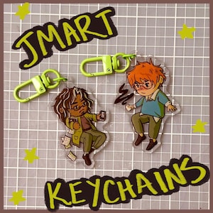 May include: Two clear acrylic keychains featuring cartoon characters with lime green lobster clasps. One character has long dark hair and glasses, holding a small object with papers. The other has short orange hair, glasses, and a blue shirt.