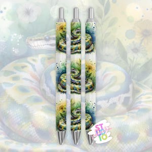 Puede incluir: Tres bolígrafos con un diseño de acuarela que presenta una serpiente enroscada y detalles florales. Los bolígrafos tienen puntas plateadas y un cuerpo blanco con una colorida ilustración de serpiente. El fondo tiene un efecto de acuarela con una serpiente y flores.