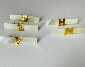 May include: Five white rectangular pieces of jewelry with gold letters D, E, H, N, and F.