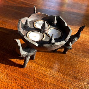May include: A wooden candle holder with four candle holders and three elephant legs. The candle holder is dark brown and has a lotus flower design.