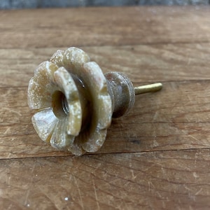 May include: A beige and brown stone flower-shaped cabinet knob with a gold metal screw.