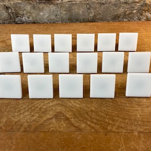 May include: Twenty white square tiles arranged in rows on a wooden surface.