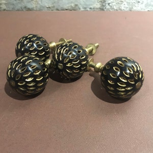 May include: Four black and gold round cabinet knobs with intricate cut-out designs. The knobs have a brass screw attachment.