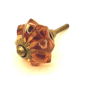 May include: Amber-colored glass cabinet knob with a faceted design. The knob has a brass-colored base and screw. This decorative hardware is suitable for drawers, cabinets, and furniture.
