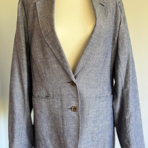 May include: A blue blazer with a two-button fastening and a notched lapel. The blazer is made of a textured fabric and has two front pockets. The blazer is displayed on a mannequin.