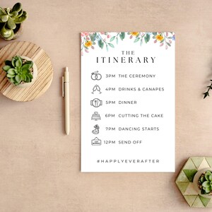 Może przedstawiać: Biała karta z planem wesela z kwiatowymi akcentami i tekstem "THE ITINERARY". Harmonogram obejmuje ceremonię, napoje, obiad, krojenie tortu, tańce i godziny odjazdu. Widoczny jest również długopis i małe rośliny doniczkowe.