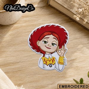 May include: Embroidered patch featuring a cartoon character with red hair, a red hat, and a white shirt with a yellow collar. The character is giving an "okay" hand gesture. The patch has a white border.
