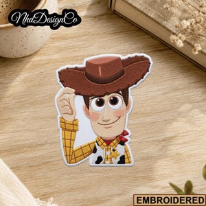 May include: Embroidered patch featuring a cartoon cowboy character with a brown hat, yellow plaid shirt, and red neckerchief. The patch has a white border and the text "EMBROIDERED" at the bottom.