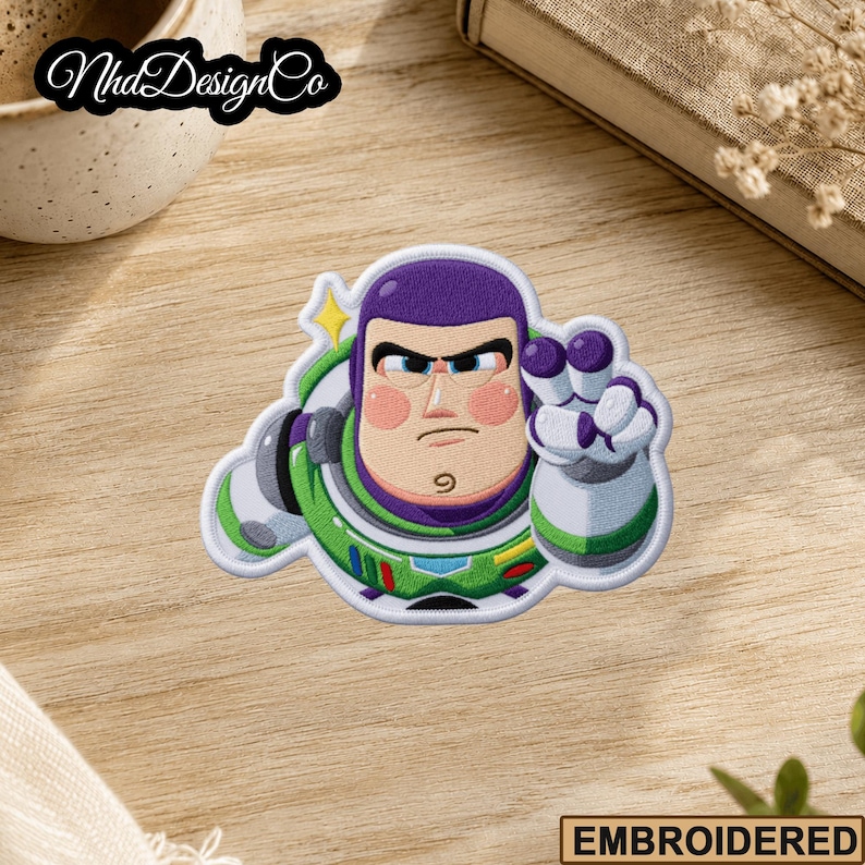 May include: Embroidered patch featuring Buzz Lightyear from Toy Story. The patch shows Buzz in his space suit with a determined expression, with green, purple, white, and red details. The patch has the word "EMBROIDERED" at the bottom.