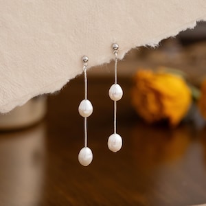 Puede incluir: Un par de pendientes de plata con tres perlas blancas en cada pendiente.