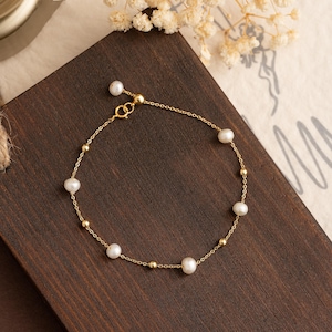 May include: A delicate gold chain bracelet featuring small white pearls and gold beads. The bracelet has a simple design and is ideal for everyday wear.