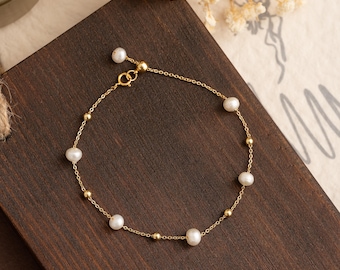 May include: A delicate gold chain bracelet with small white pearls and gold beads. The bracelet has a simple design and is perfect for everyday wear.