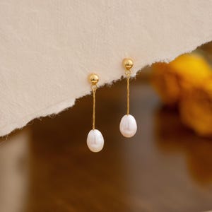 May include: A pair of gold drop earrings with a single white pearl dangling from each earring.