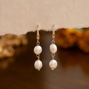 May include: A pair of gold earrings with two white pearl drops on each earring.