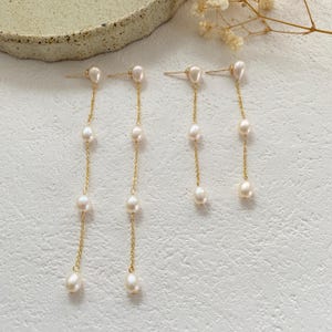 Könnte beinhalten: Ein Set aus vier goldenen Kettenohrringen mit Perlenakzenten. Jeder Ohrring hat eine einzelne Perle oben und vier Perlen, die an der Kette herunterhängen.