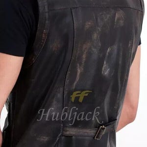 May include: A distressed black leather vest with a buckle closure. The vest has a worn, vintage appearance with visible texture and subtle color variations. The text "FF Hubljack" is printed on the lower back.