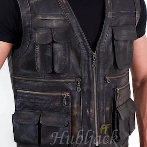 May include: A distressed black leather vest with multiple pockets and a front zipper closure. The vest has a worn, vintage appearance, with visible wear and tear. The text "Hubljack" is visible on the lower right side of the vest.