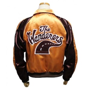 Peut inclure: Une veste bomber en satin marron et or avec les mots "The Wanderers" brodés au dos. La broderie comprend une route stylisée.