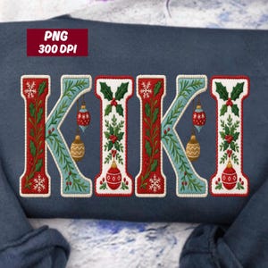 May include: A navy blue sweatshirt featuring the name "KIKI" in a festive, embroidered design. Each letter is outlined in red and white, with blue accents and Christmas ornaments. The letters are decorated with holly and snowflakes.