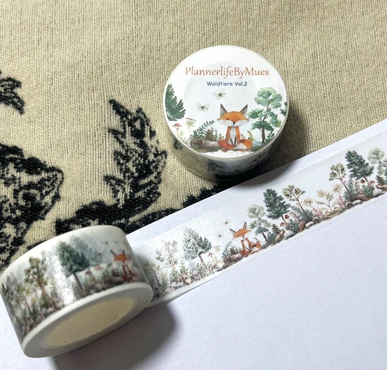 Op de afbeelding: Een rol washi tape met een bosmotief. De tape heeft een vos, bomen en paddenstoelen. De tape is gelabeld "PlannerlifeByMues Waldtiere Vol. 2".