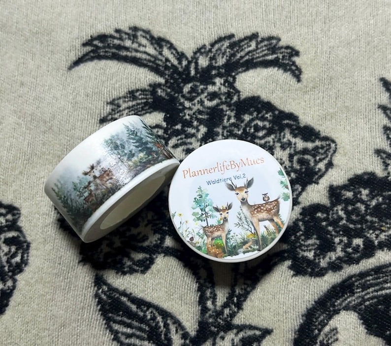 Op de afbeelding: Een rol washi tape met een boslandschap met herten, een vogel en bomen. De tape is gelabeld "PlannerlifeByMues" en "Wildtiere Vol. 2".