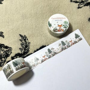 Op de afbeelding: Twee rollen washi tape met een bosmotief. De tape heeft een vos, bomen en andere bosselementen. De tape is gelabeld "PlannerlifeByMues Wildfire Vol. 2".