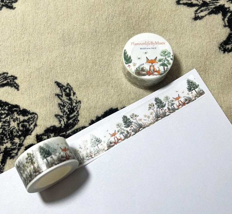 Op de afbeelding: Twee rollen washi tape met een bosmotief. De tape heeft een vos, bomen en andere bosselementen. De tape is gelabeld "PlannerlifeByMues Wildfire Vol. 2".
